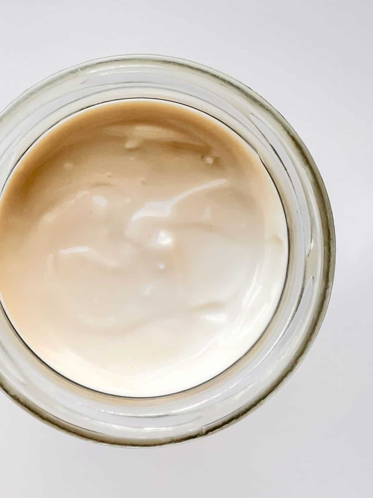 A close up image of a jar of baked milk yogurt against a white countertop.