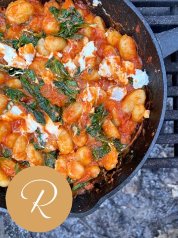An image of cooked Smoky Gnocchi in a cast iron pan on a grate over an open fire.