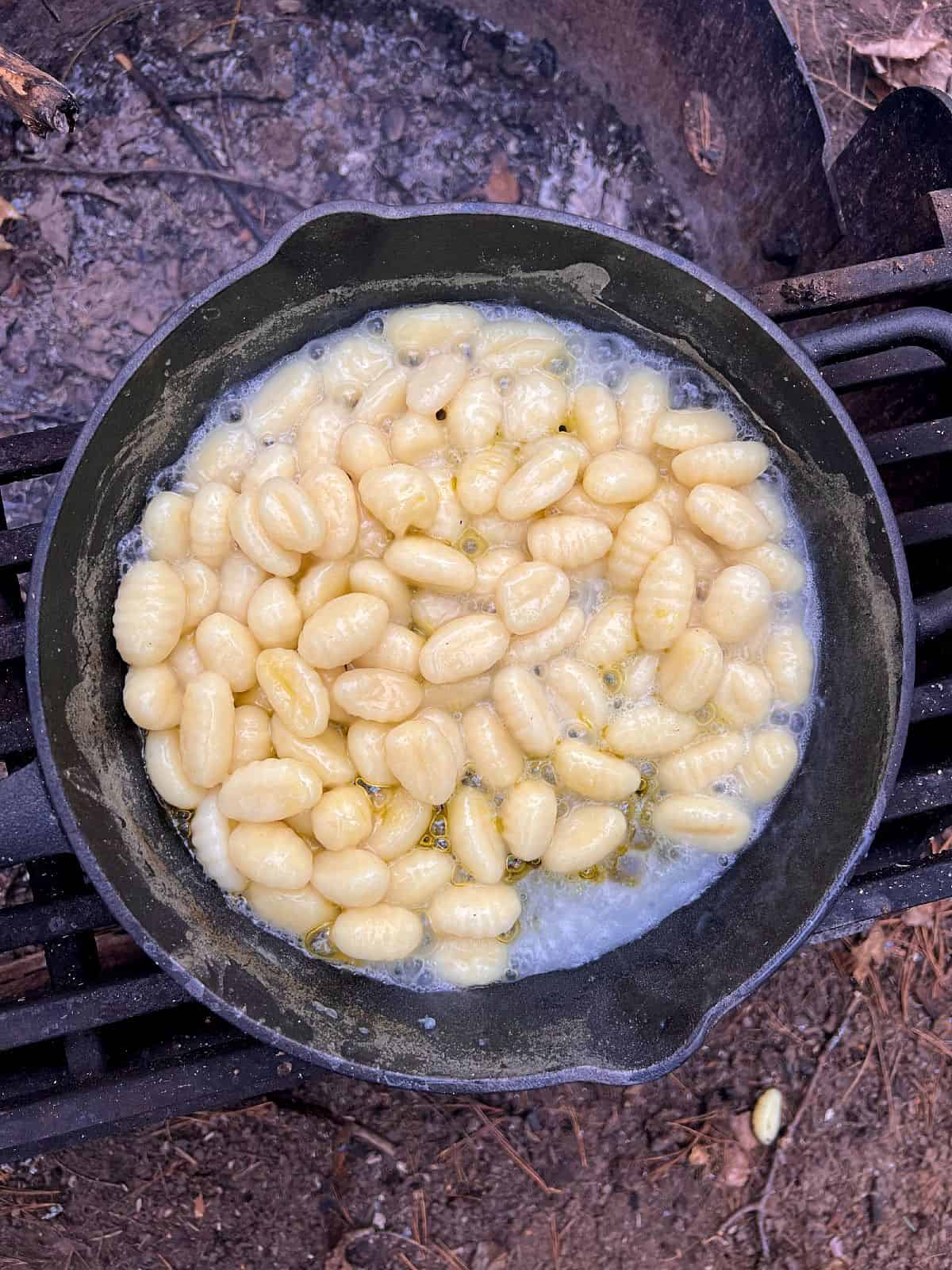 An image of gnocchi cooking in boiling water in a cast iron pan over an open fire.