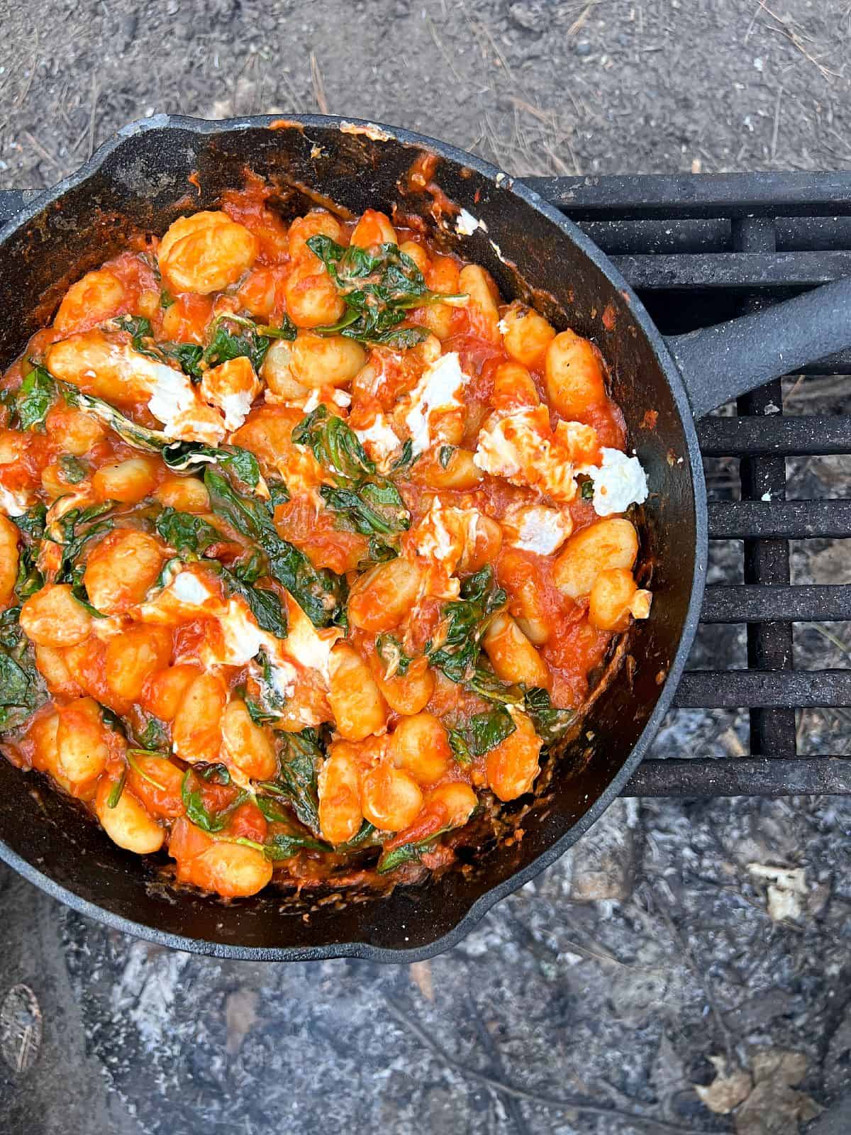 An image of cooked Smoky Gnocchi in a cast iron pan on a grate over an open fire.