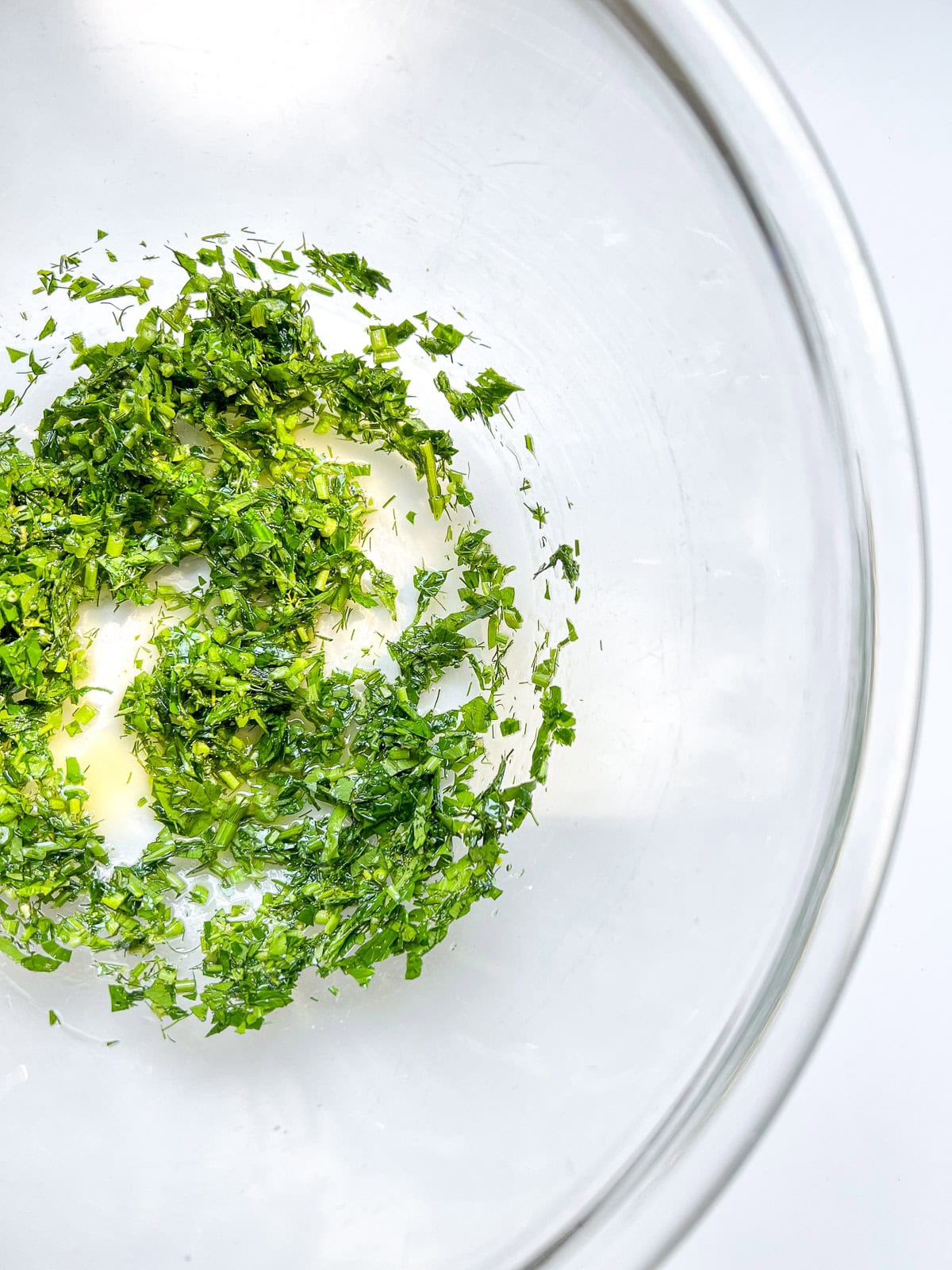 An image of herbs, lemon juice, and olive oil in the bottom of a glass bowl.