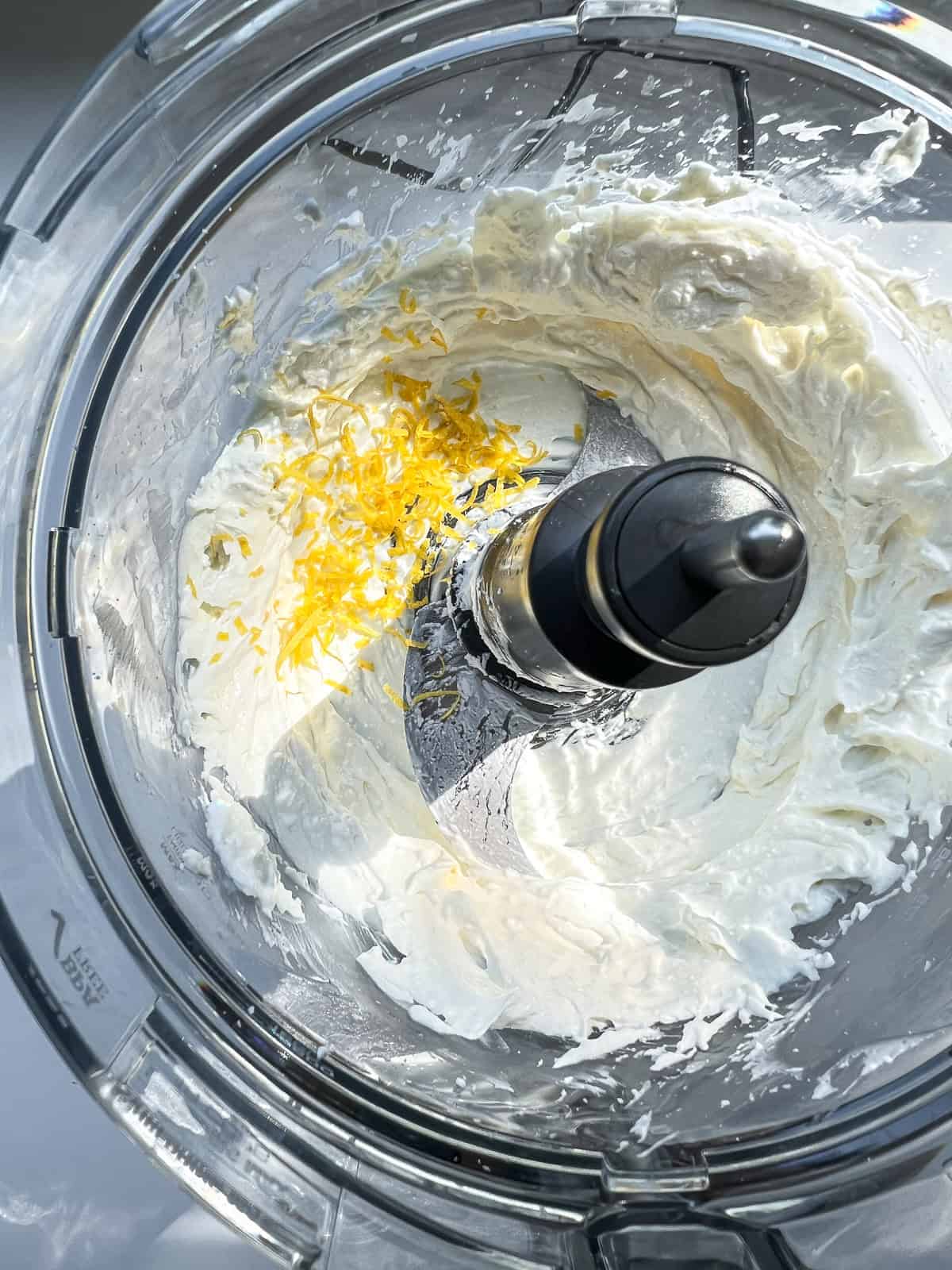 An image of feta, labneh, and garlic in the bowl of a food processor.