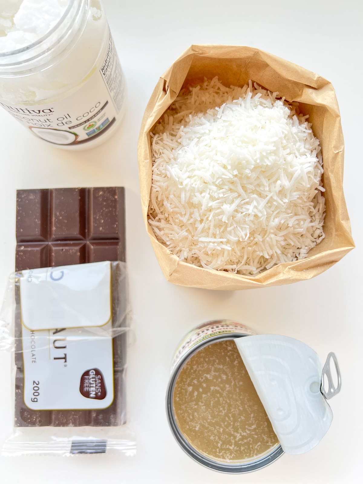 An image of the ingredients needed for Chocolate Coconut Bonbons, which includes a bar of dark chocolate, shredded coconut, condensed coconut milk, and coconut oil.
