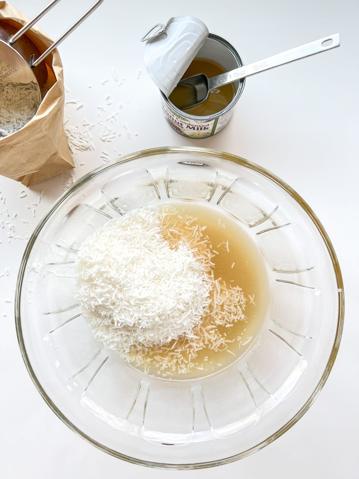 An image of the first step of making Chocolate Coconut Bites, showing a glass bowl containing the coconut and the condensed milk.