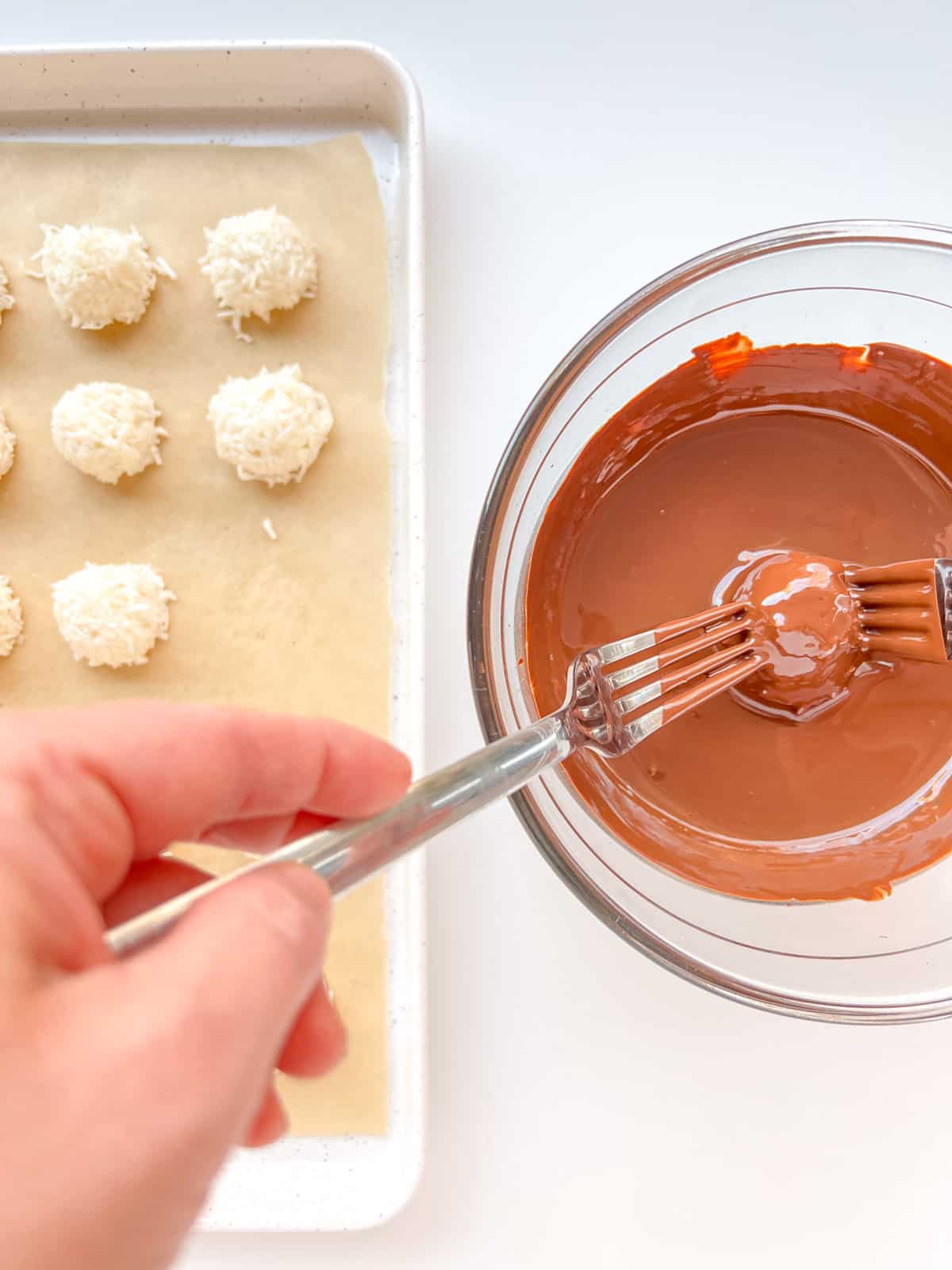 An image of the chilled coconut centres being dipped into a bowl of melted chocolate.