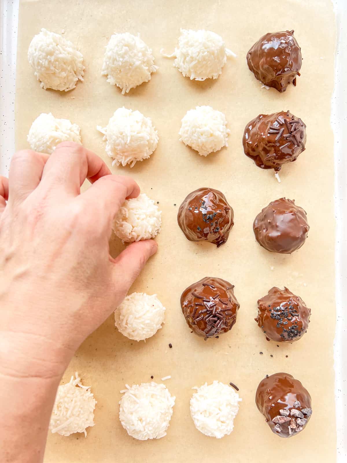 An image of a hand picking up a coconut bonbon from a tray filled with bonbons being made.