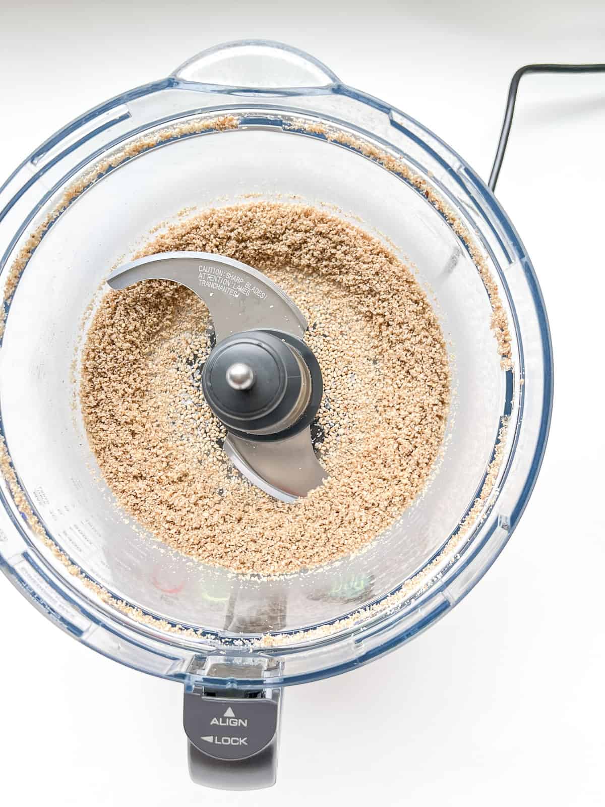 A close up of the bowl of a food processor containing ground sesame seeds and salt.