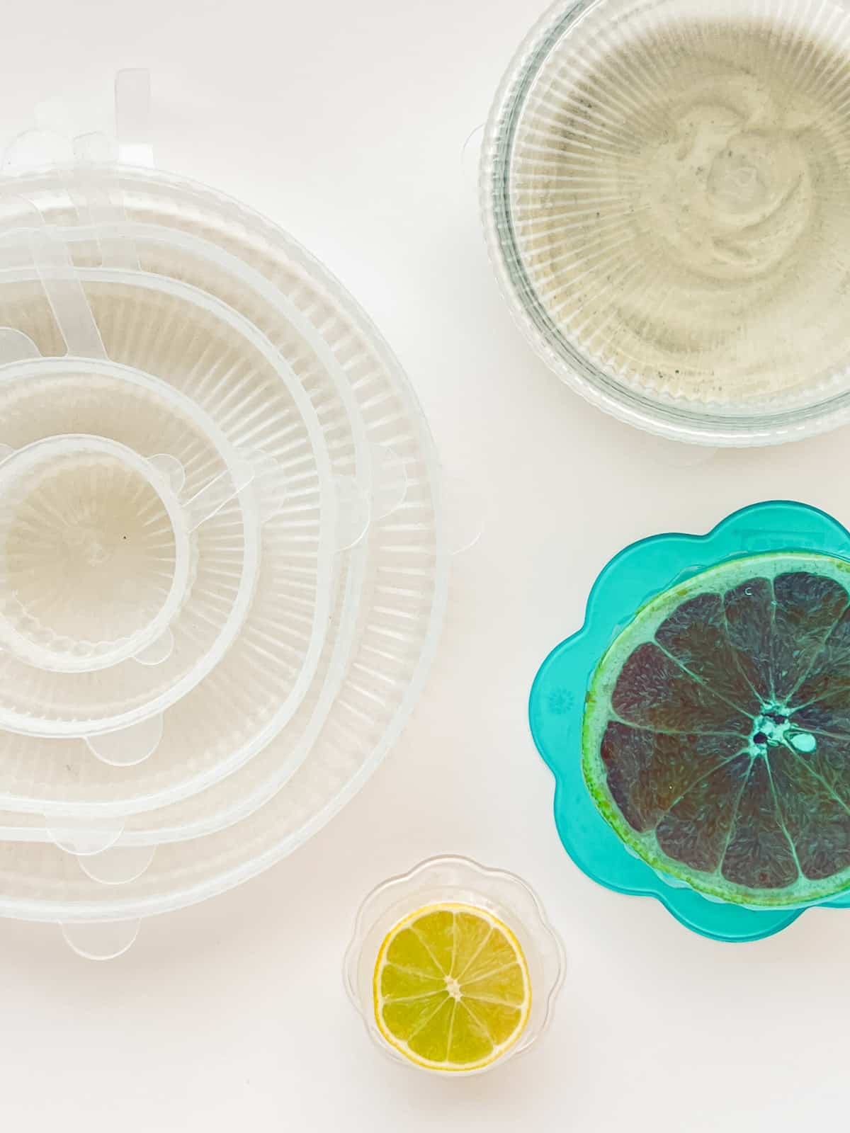 An image of a selection of different kinds of silicone stretch lids, including a few that are covering cut citrus fruit and one that is covering a glass bowl.