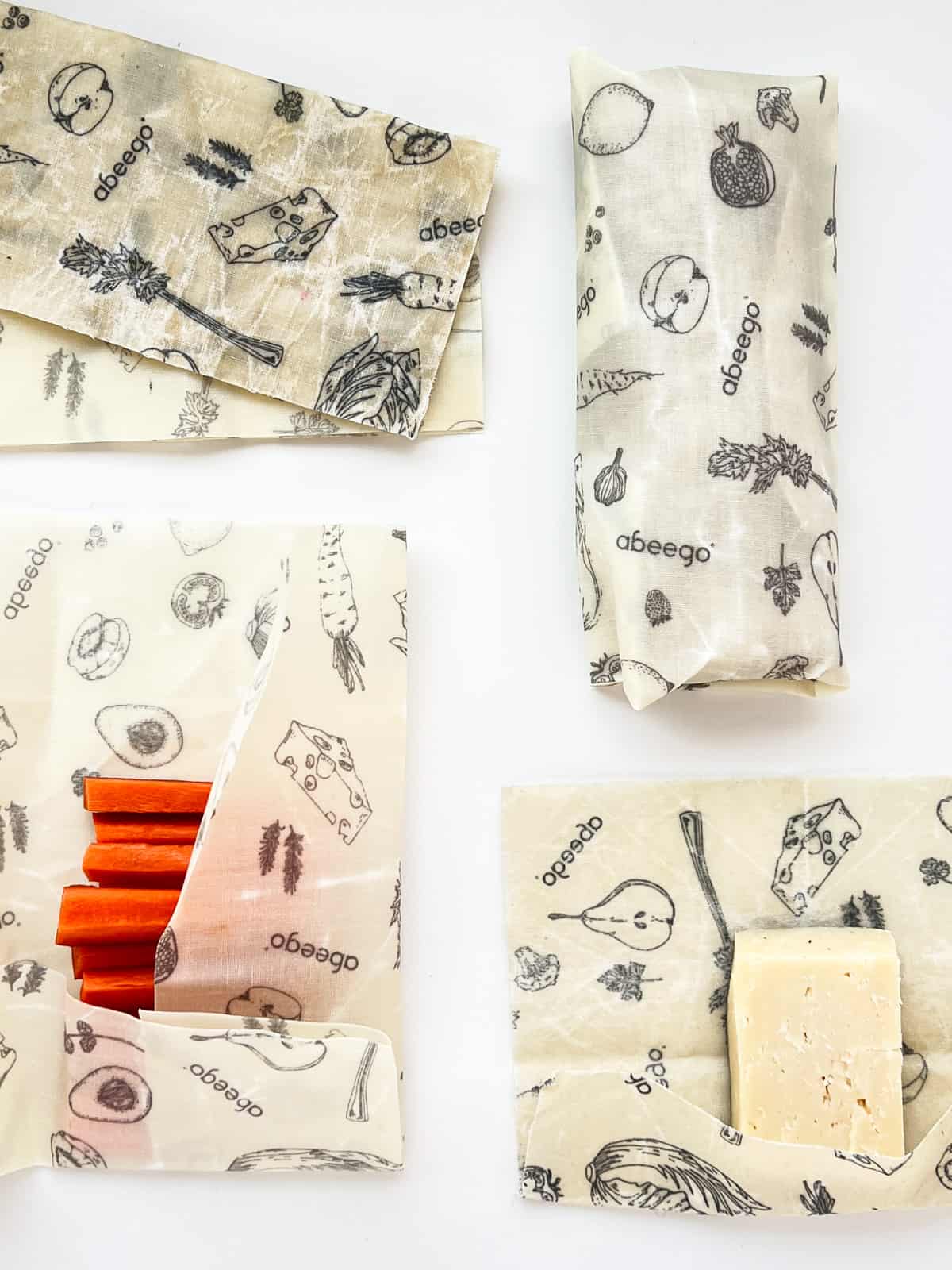 An image of various sizes of beeswax wraps, wrapping cut carrot sticks, cheese and a burrito.