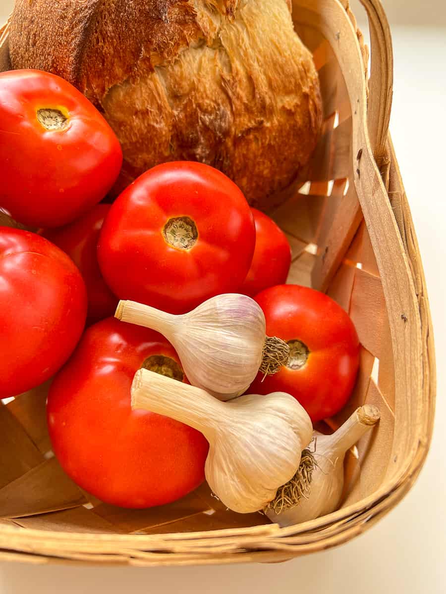 An image of tomatoes, garlic and bread in a woven basket.