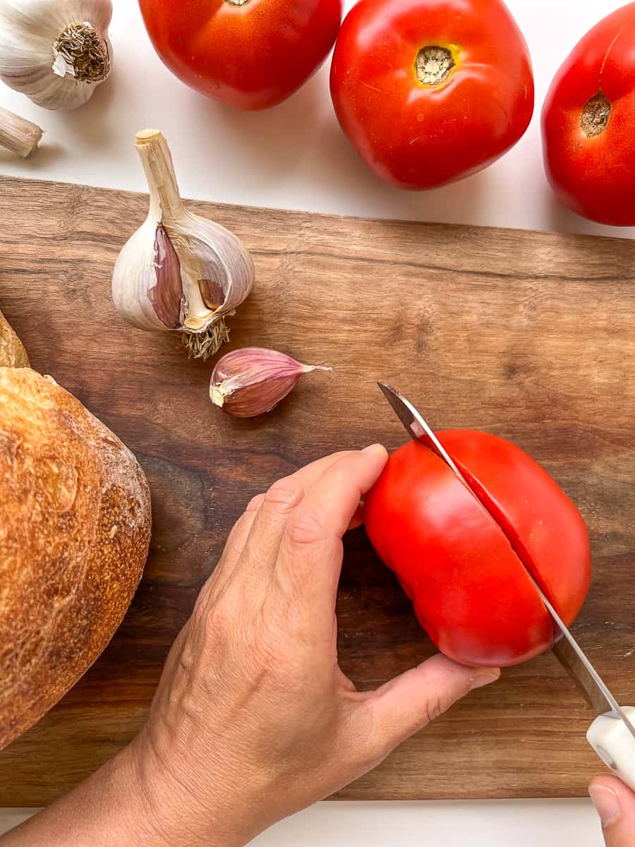 An image of a woman's hand cutting a tomato in half.