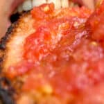 A close up image of a piece of pan con tomate near a woman's mouth, about to be eaten.