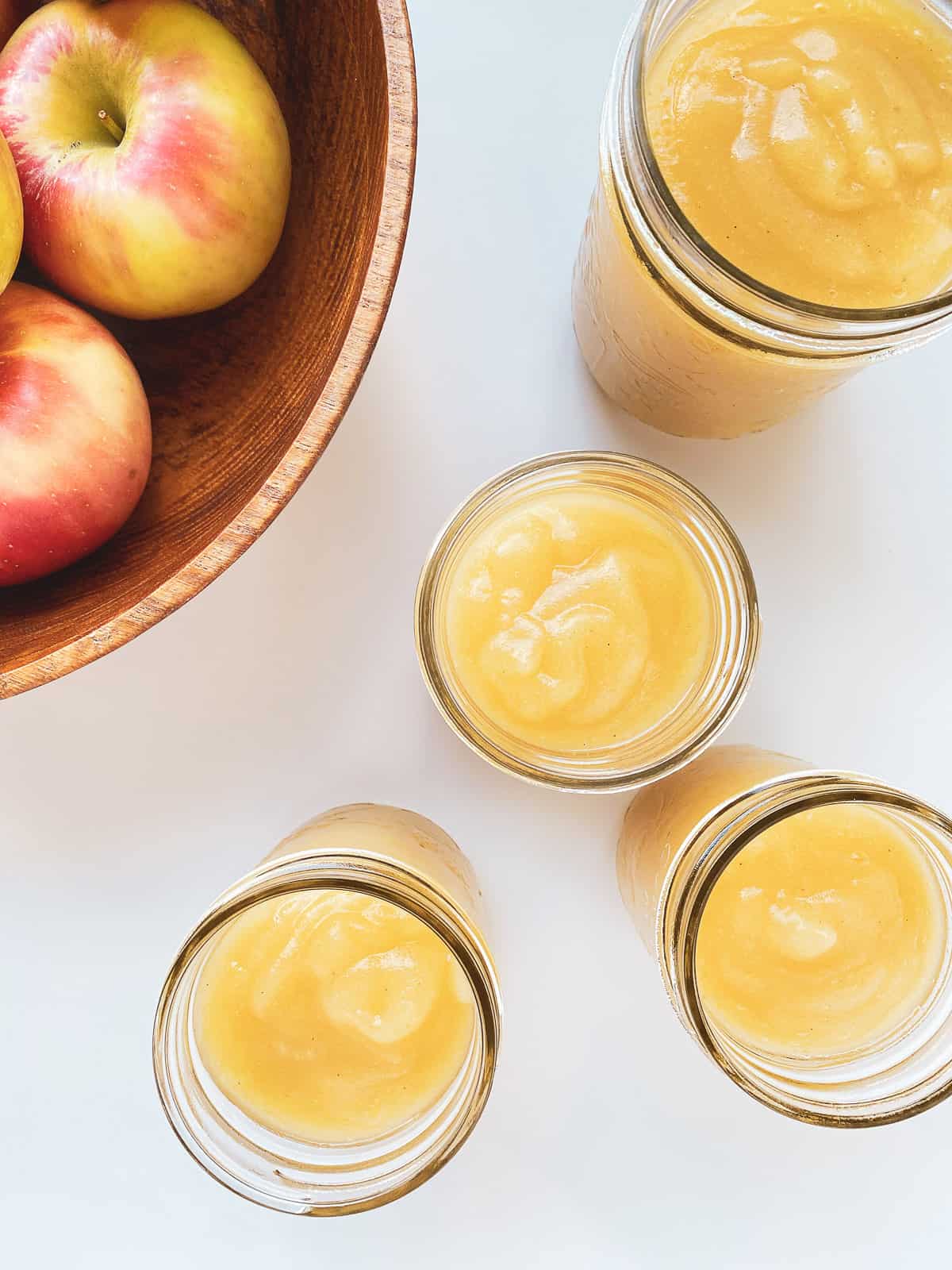 An image of homemade applesauce in glass jars on a white countertop.