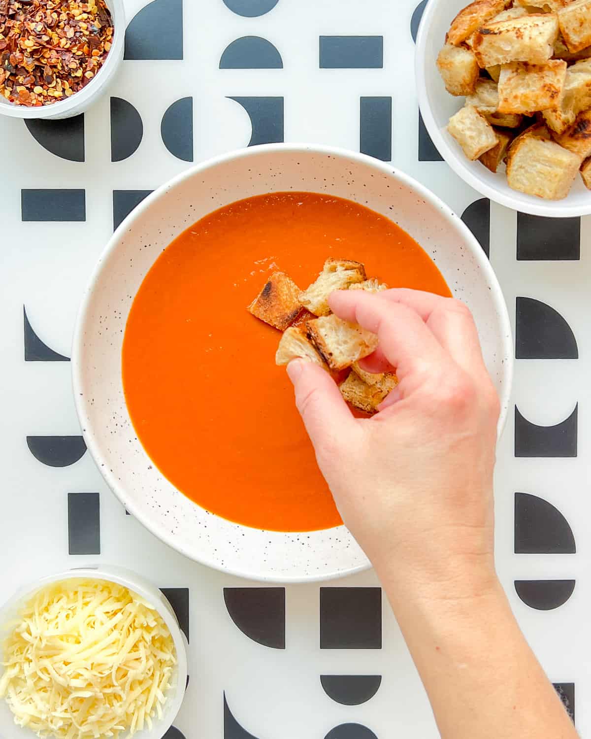 An image of roasted tomato soup being garnished with croutons.