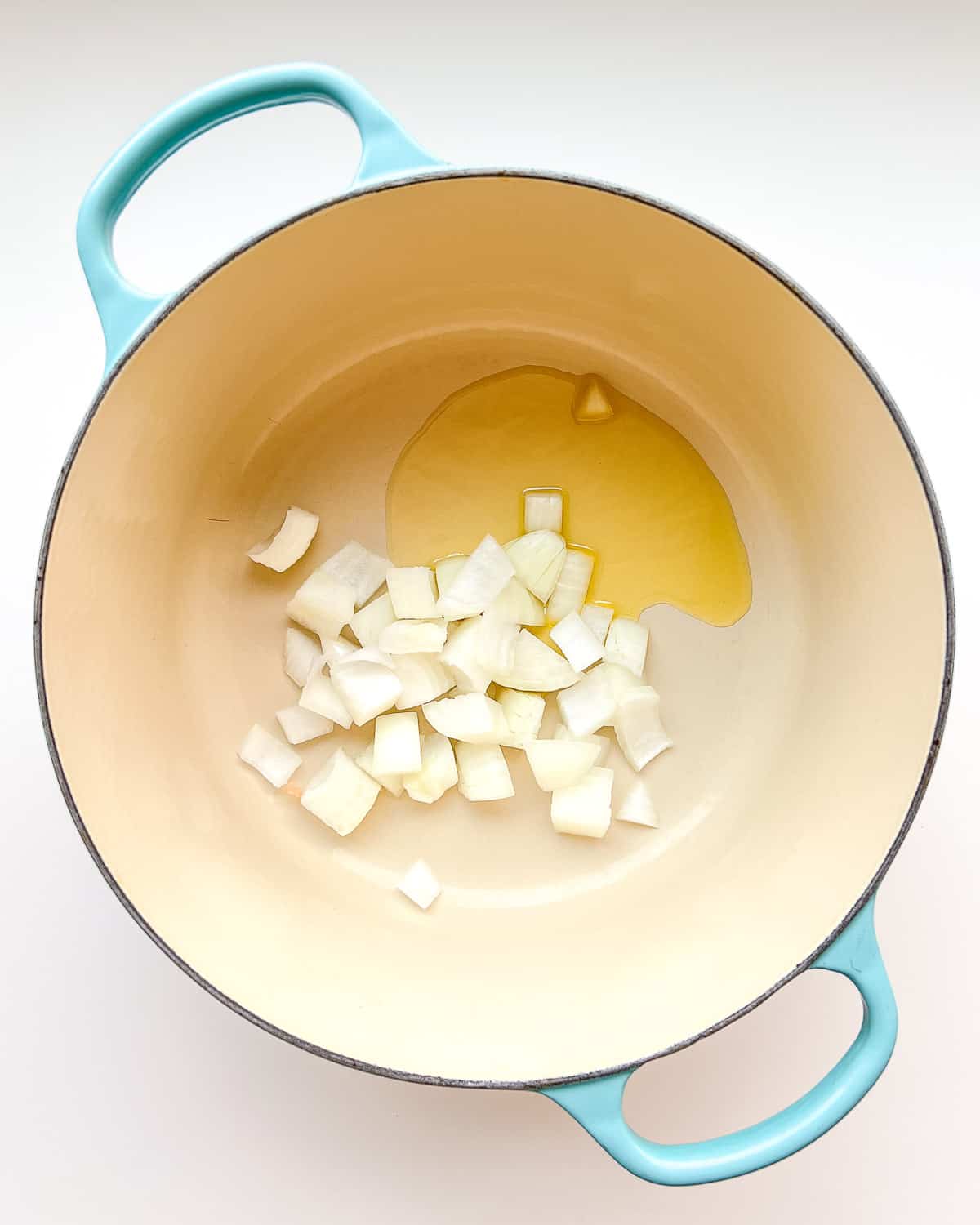 An image of diced onions and olive oil in a soup pot before being cooked.