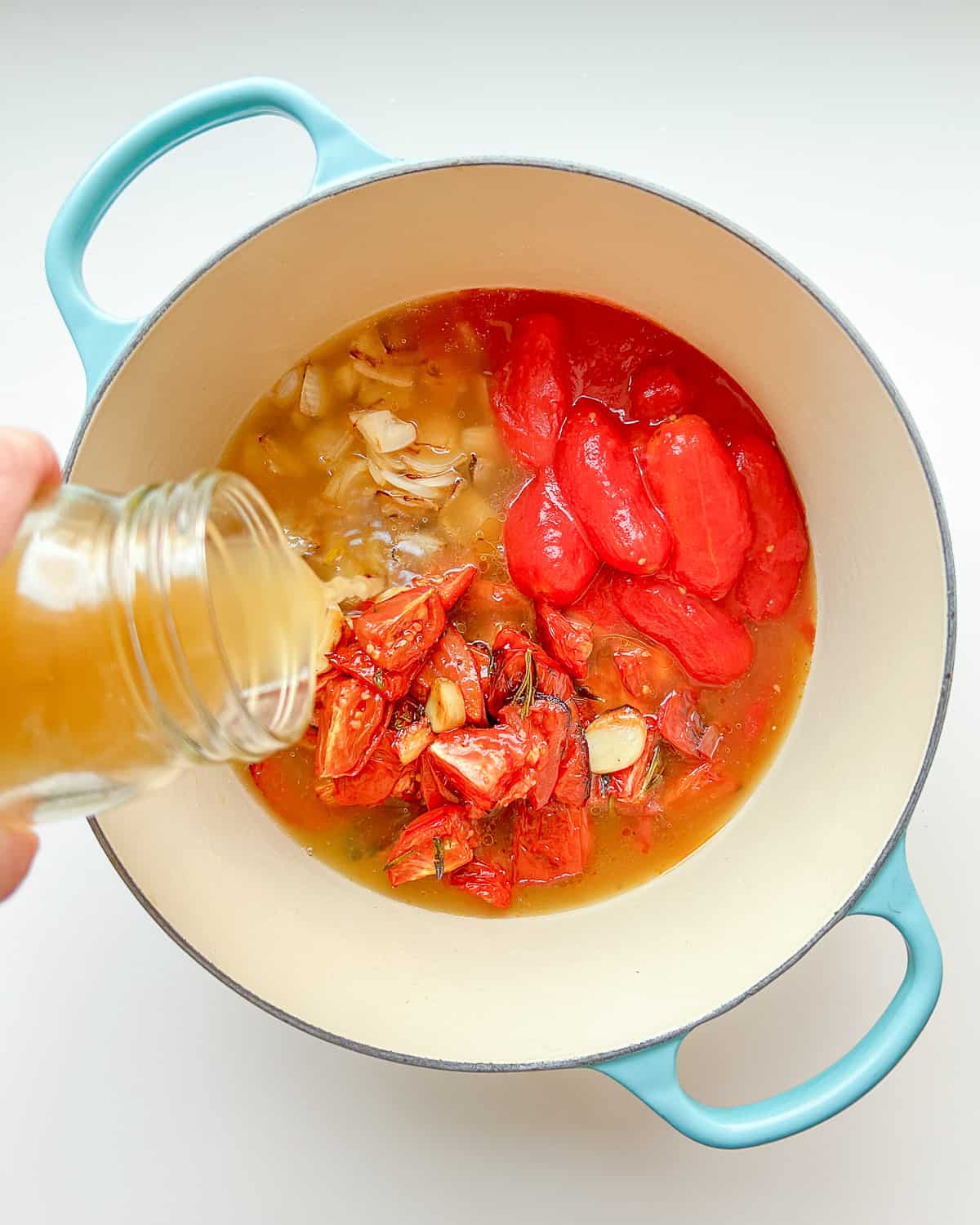 An image of vegetable broth being poured into a pot containing all of the ingredients needed for Roasted Tomato and Garlic soup before being cooked.