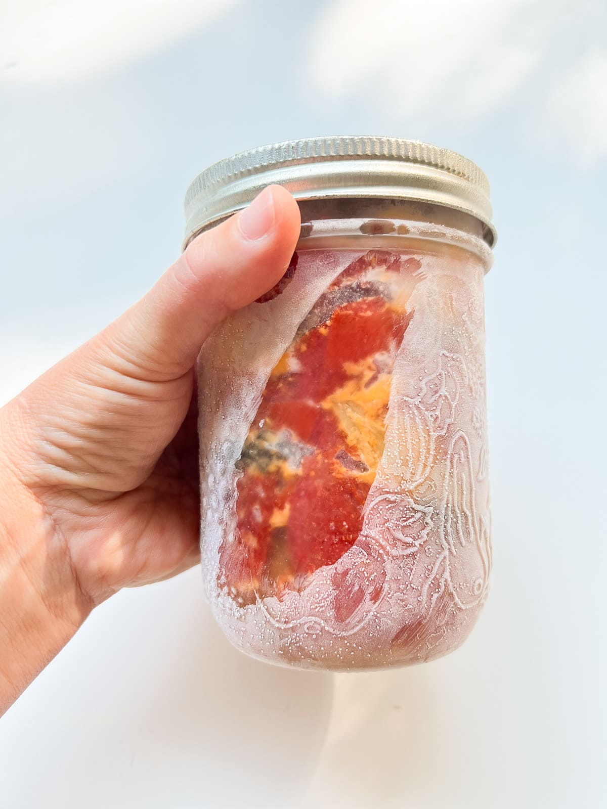 An image of half a batch of Oven Roasted Tomatoes frozen in a glass jar - the jar is being held by a woman's hand.