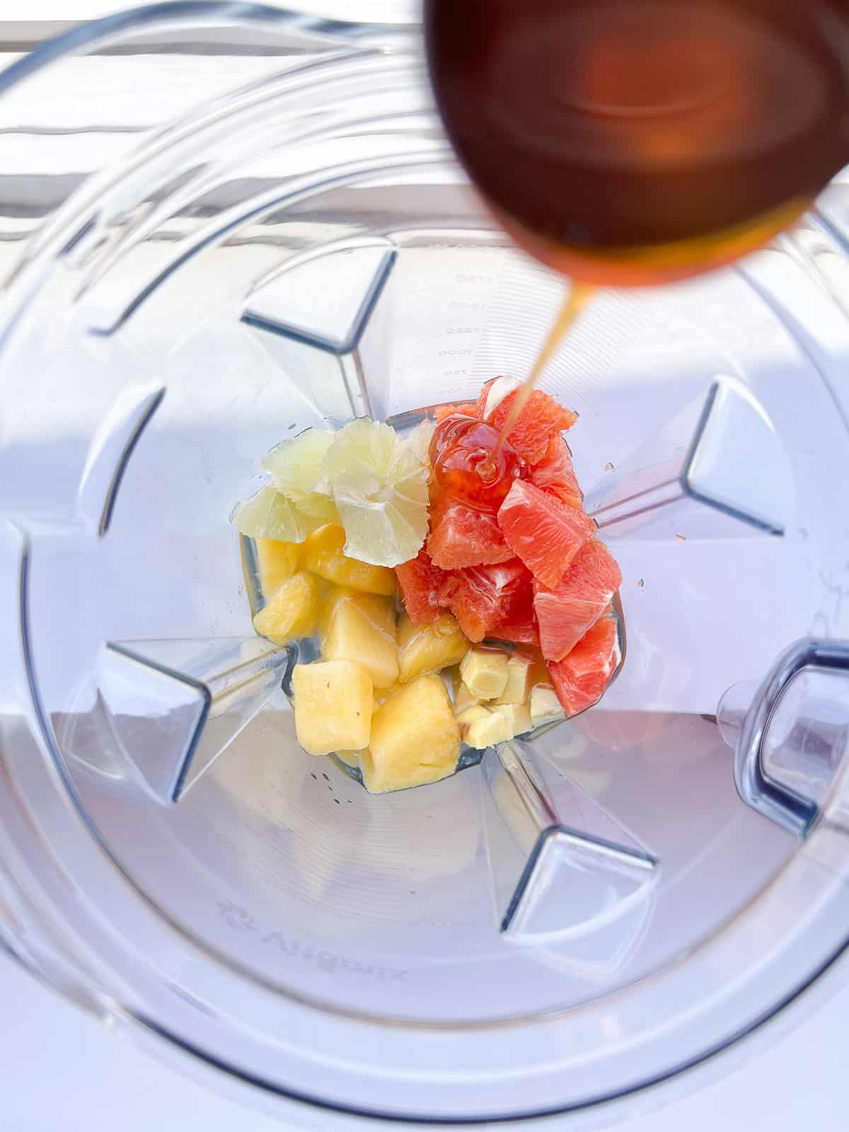 Fruit inside a blender cannister ready to be blended, with honey being drizzled in from a spoon.