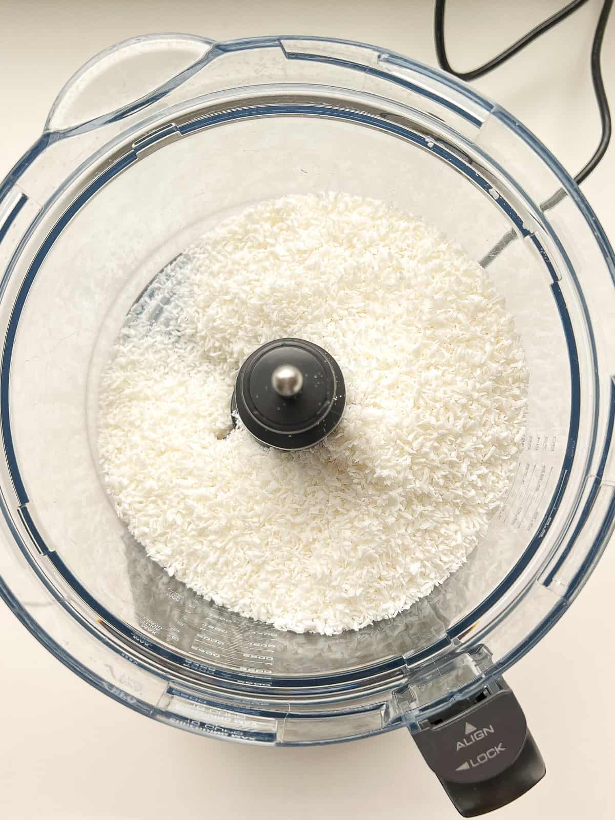 An image of shredded coconut inside the canister of a food processor.