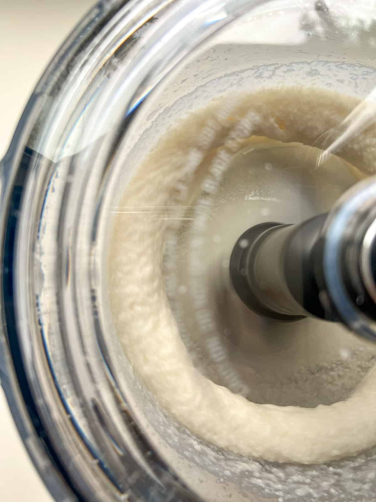 An image of shredded coconut being processed into coconut butter.