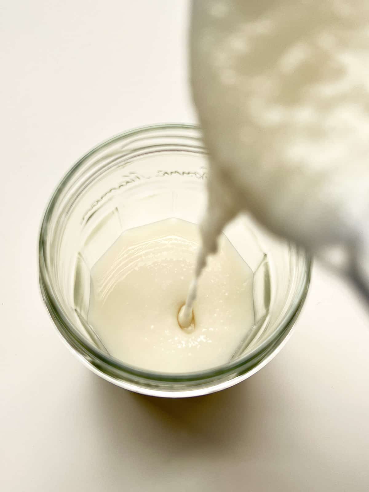 An image of coconut butter being poured into a glass jar.