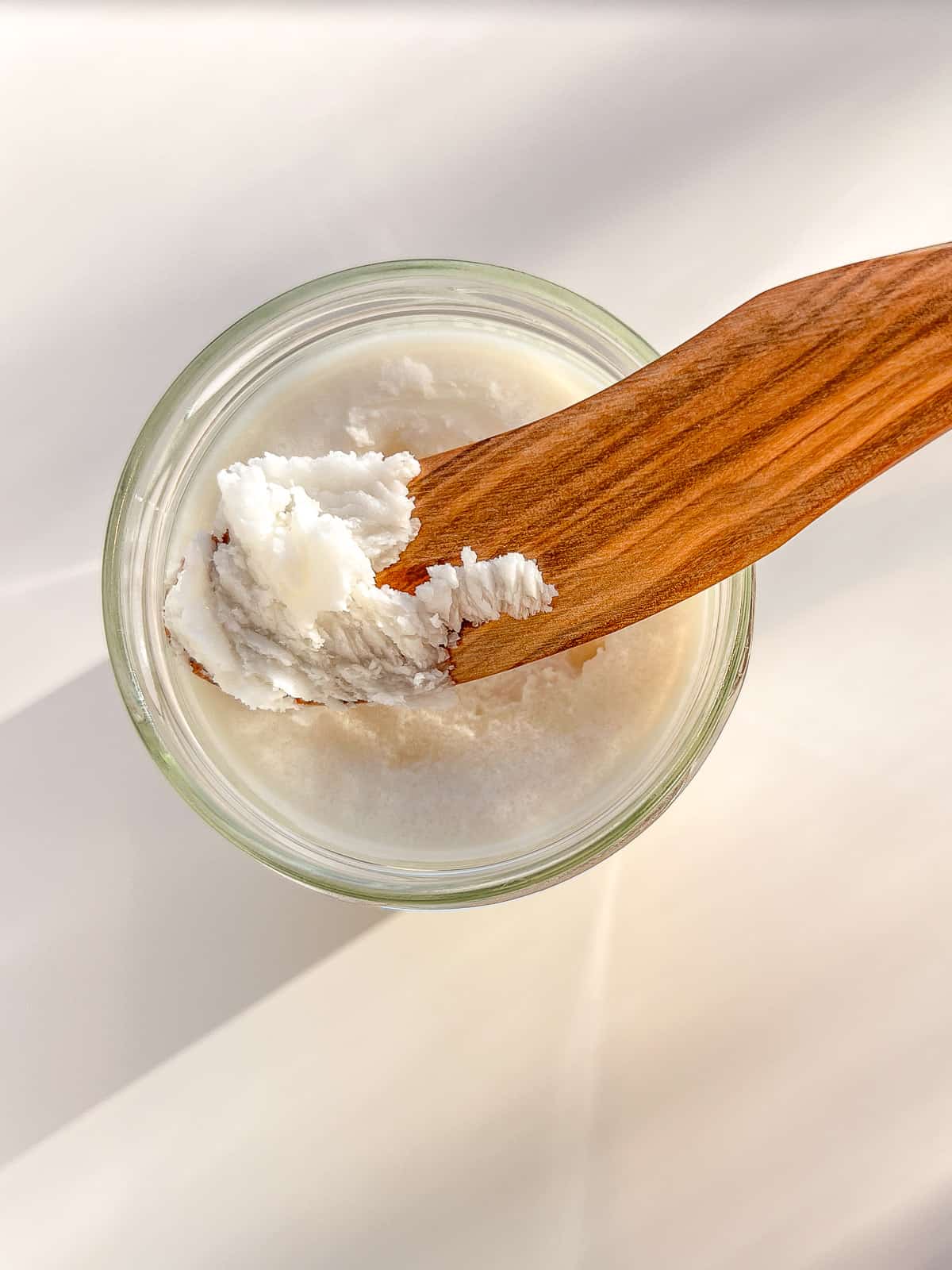 An image of coconut butter in a glass jar with a wooden spreader perched on top.
