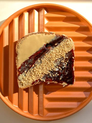 An image of Date Sesame Crunch Toast on an orange coloured plate against a white background.