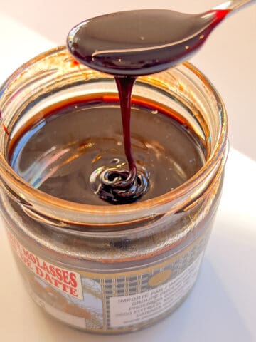 An image of date syrup being drizzled off a spoon over a full jar.