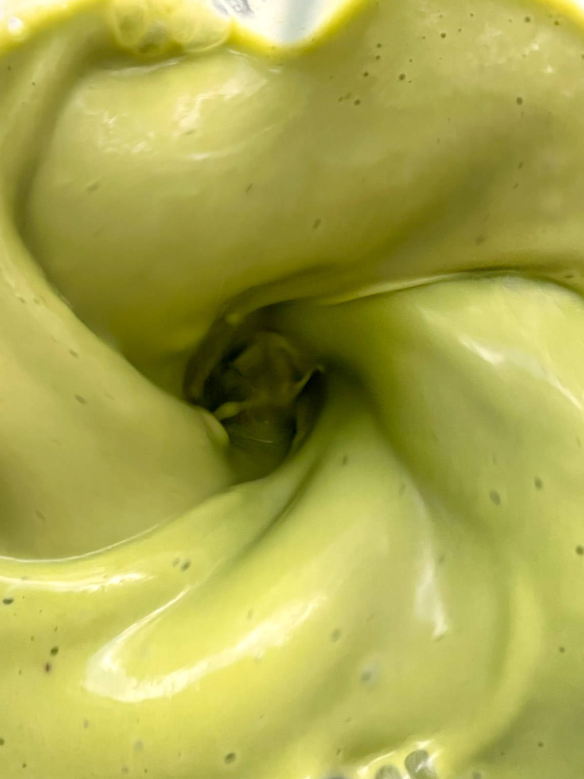 A close up image of a green smoothie in a blender canister as it is being blended.
