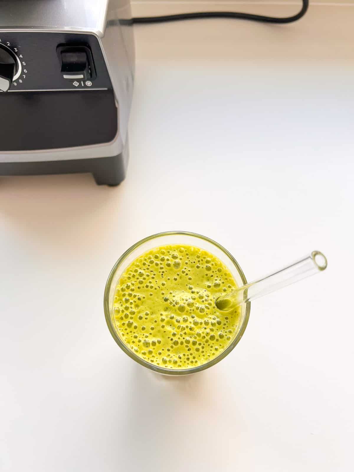 An image of a green smoothie on a white counter with the blender in the background.