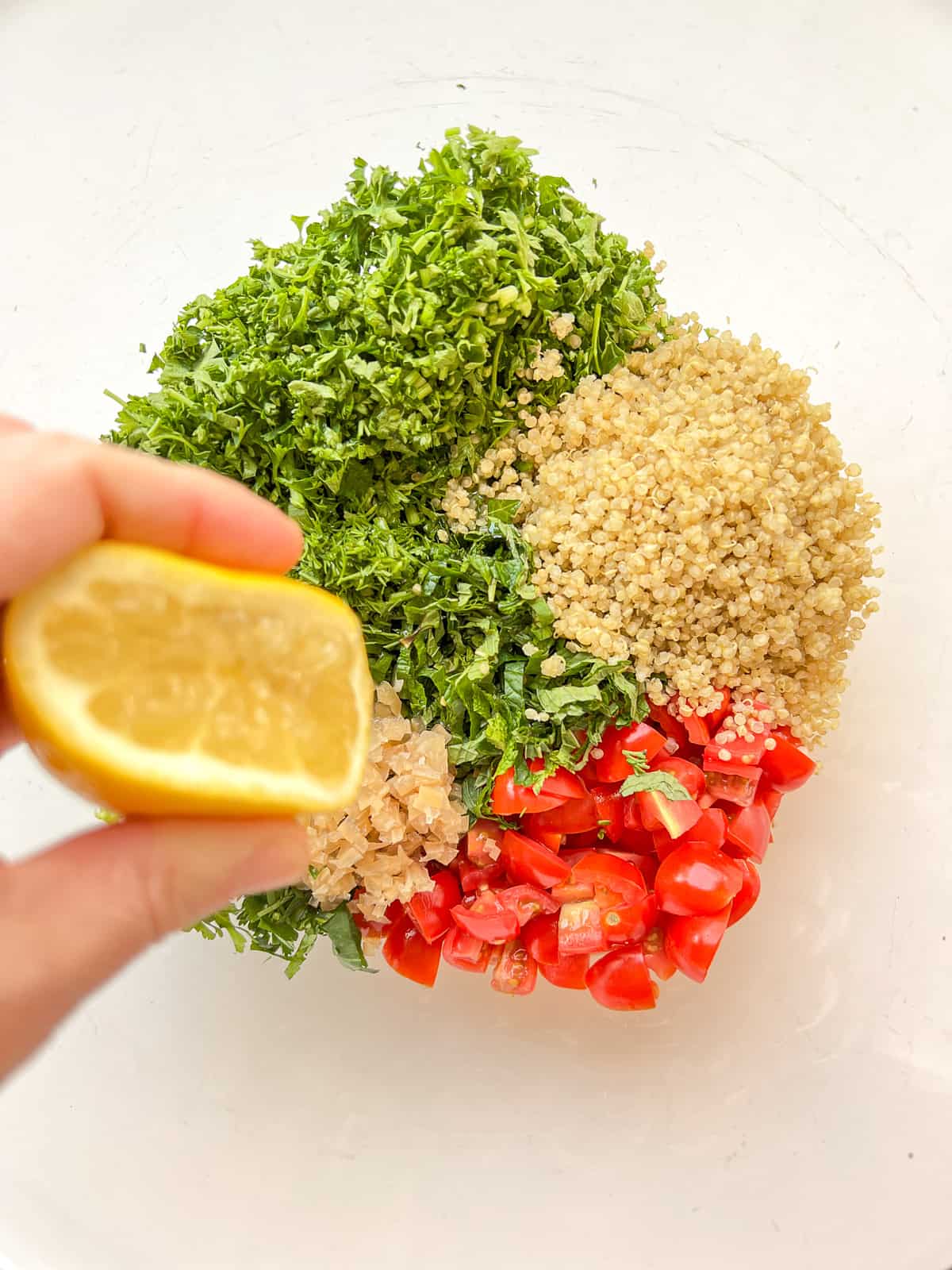 Lemon being squeezed into a bowl containing the ingredients for tabbouleh.