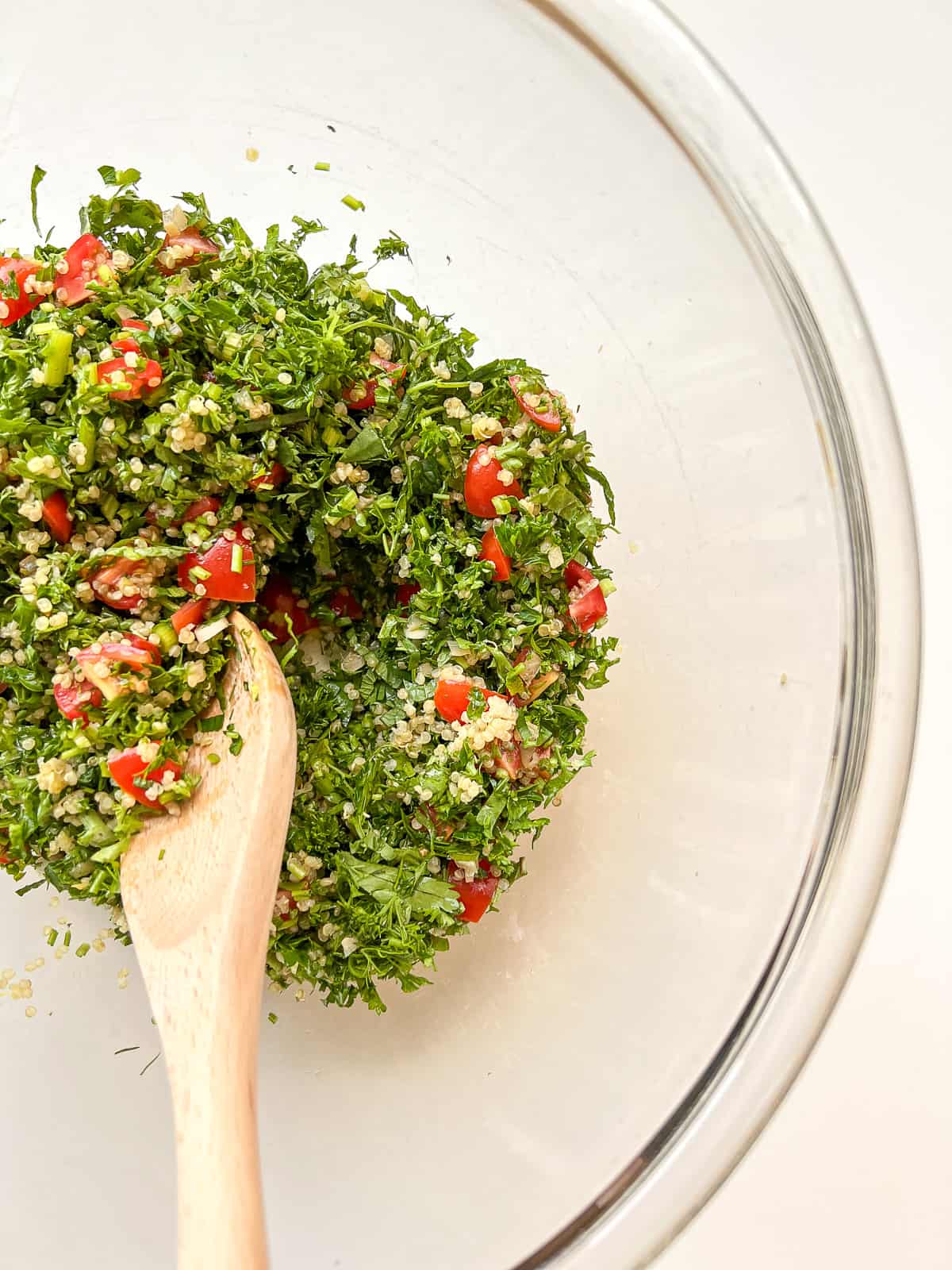 An image of tabbouleh being mixed in a glass mixing bowl.