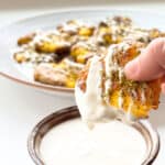 An image of a crispy smashed potato being dipped into tahini.