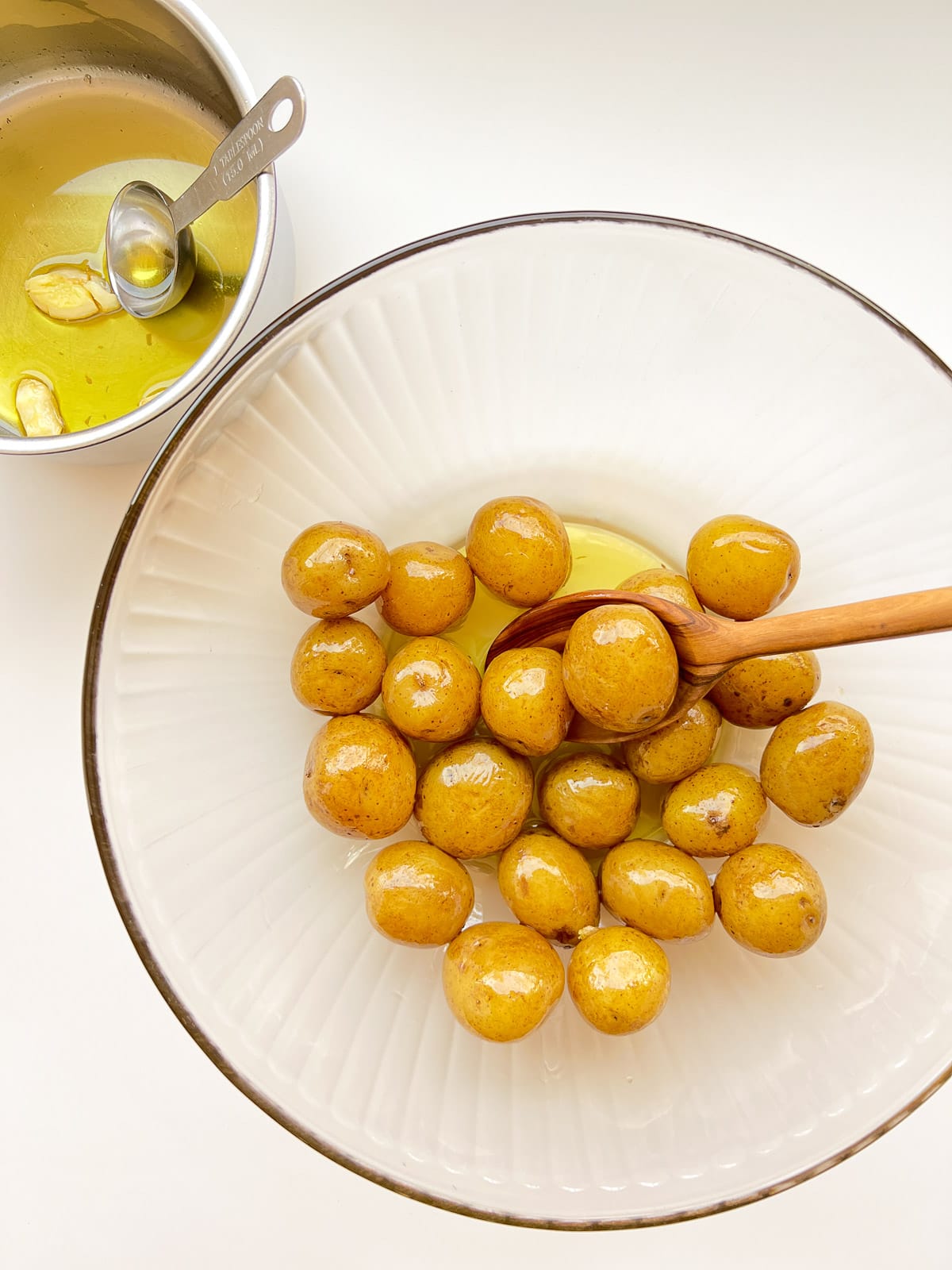 An image of small potatoes being tossed with oil in a large glass bow.