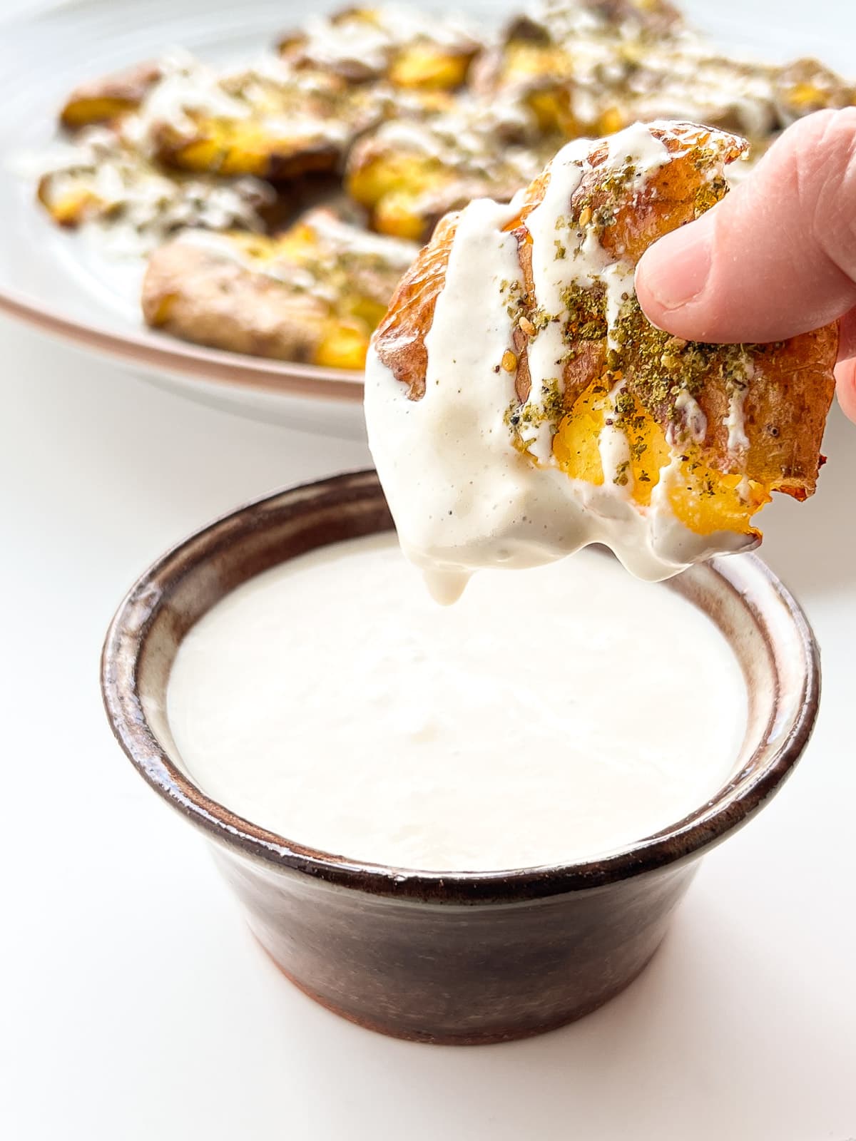 An image of a crispy smashed potato being dipped into tahini.