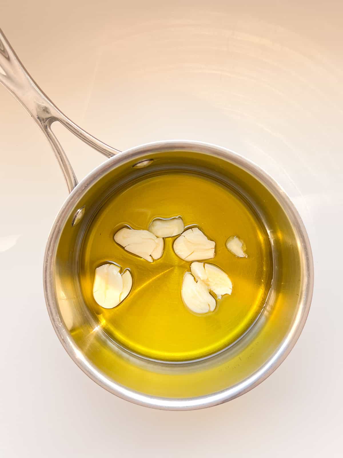 An image of oil and garlic in a small stainless steel pot.