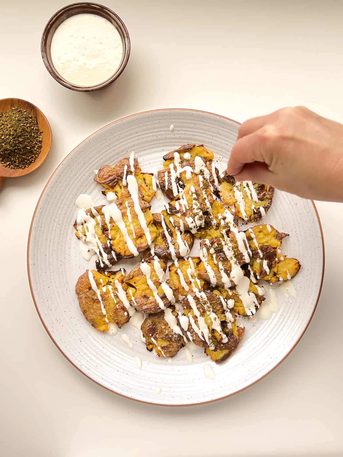 An image of a hand sprinkling za'atar onto crispy smashed potatoes.