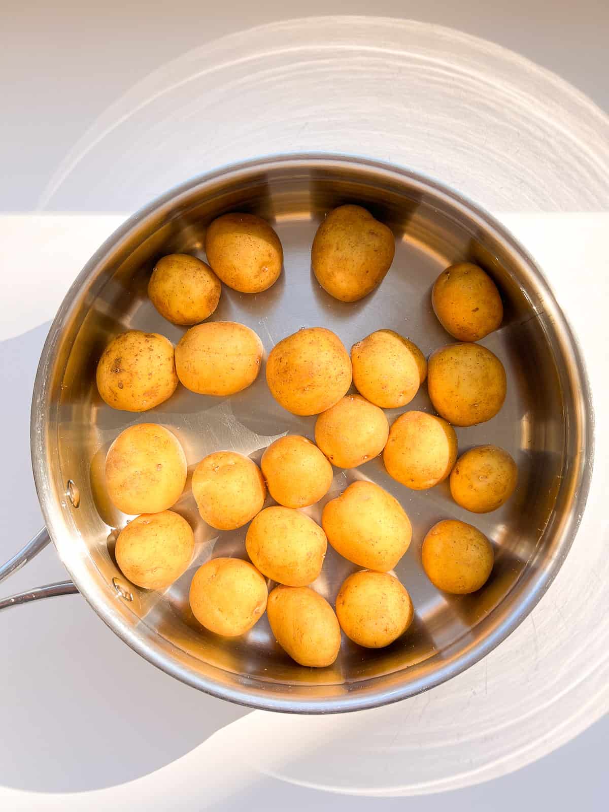 An image of small potatoes being boiled in a wide stainless steel pot.