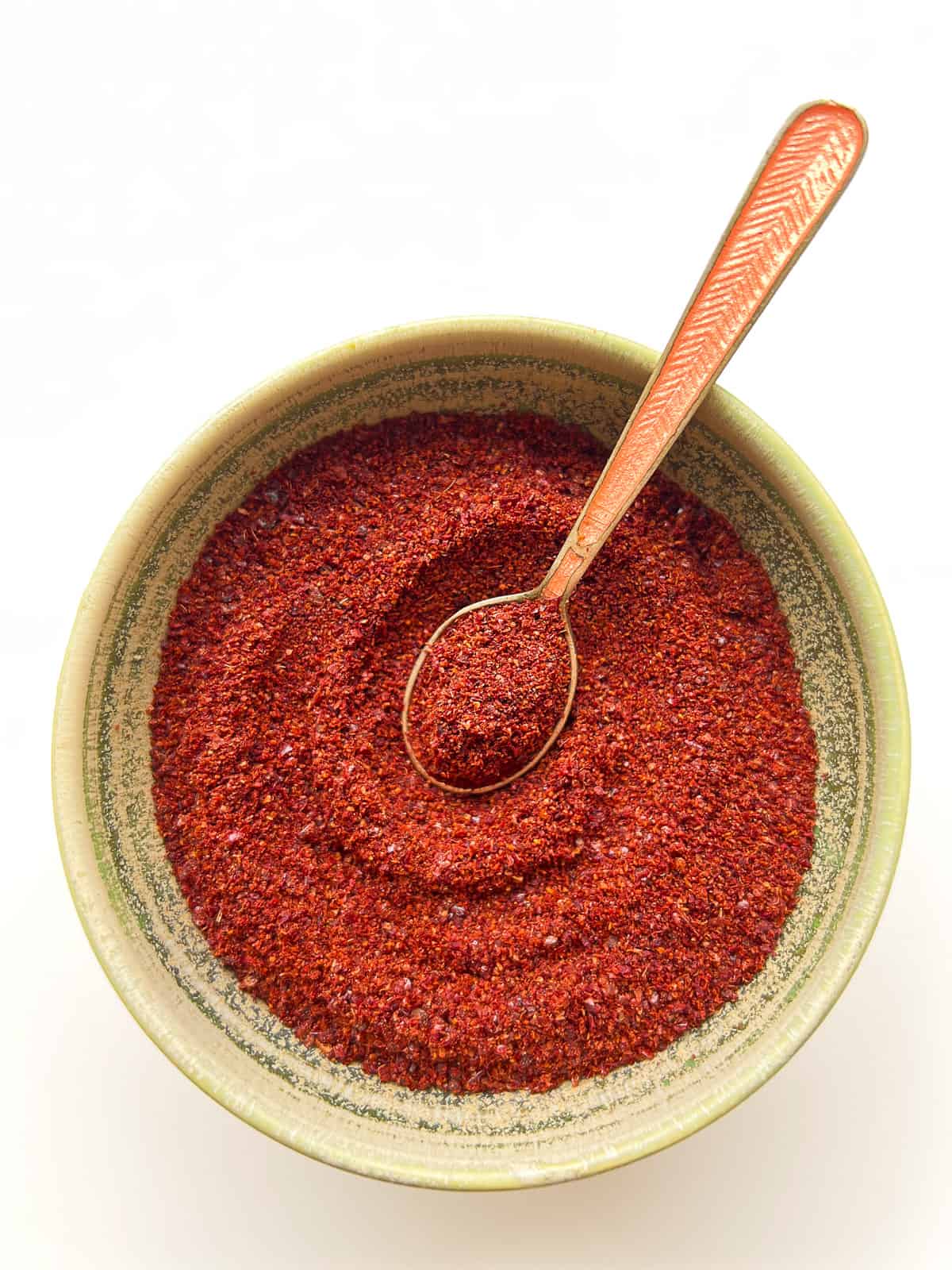 An image of ground dried sumac in a bowl with a small spoon.