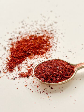 An image of ground dried sumac on a small spoon and scattered in the background.