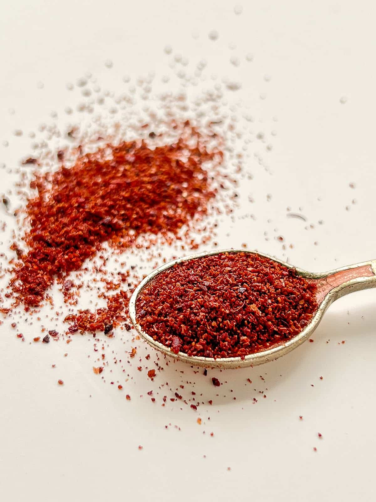 An image of ground dried sumac on a small spoon and scattered in the background.