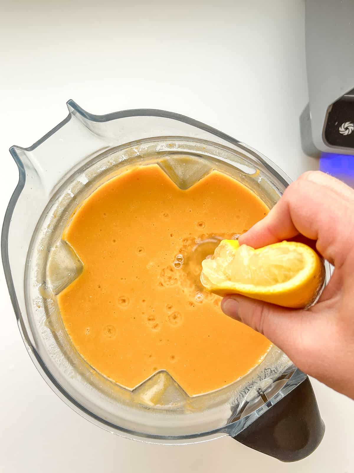 An image of lemon being squeezed into a blender full of lentil soup.