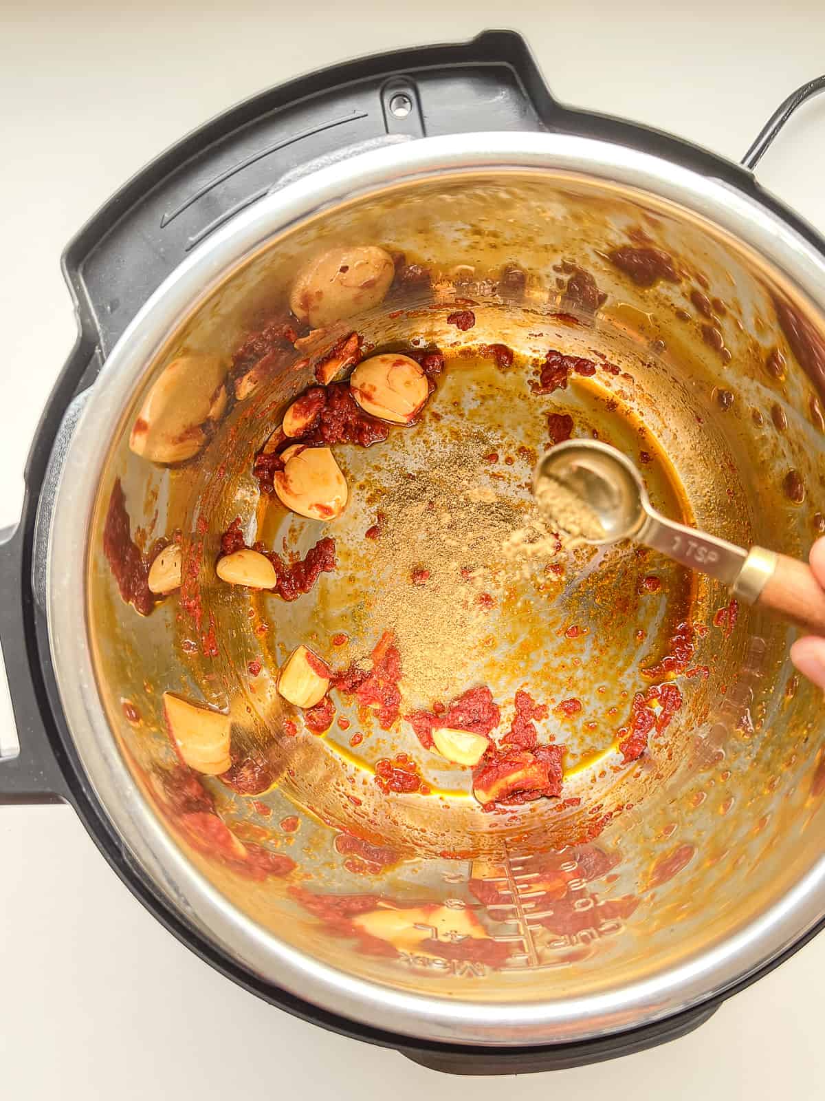 An image of garlic and tomato paste in the inner bowl of an instant pot.