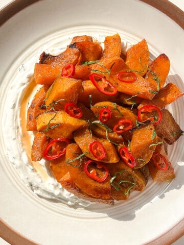 An image of Roasted squash with warm spices, pickled chilies, and lemon mint labneh on a white ceramic plate against a white background.