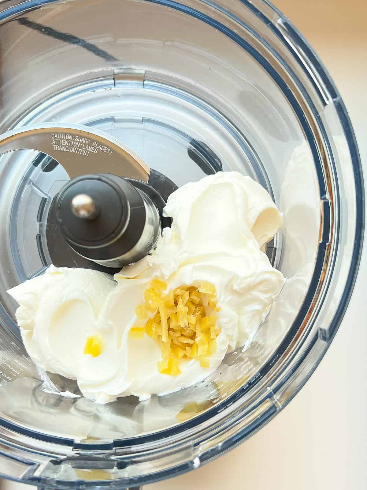 An image of preserved lemon and labneh in the bowl of a food processor.