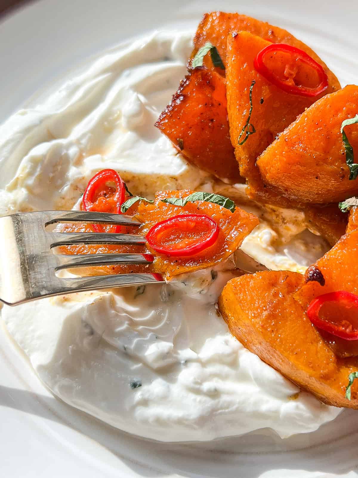 A close up image of the labneh mixture on a plate underneath the roasted squash, with a brass fork about to take a piece off the plate.