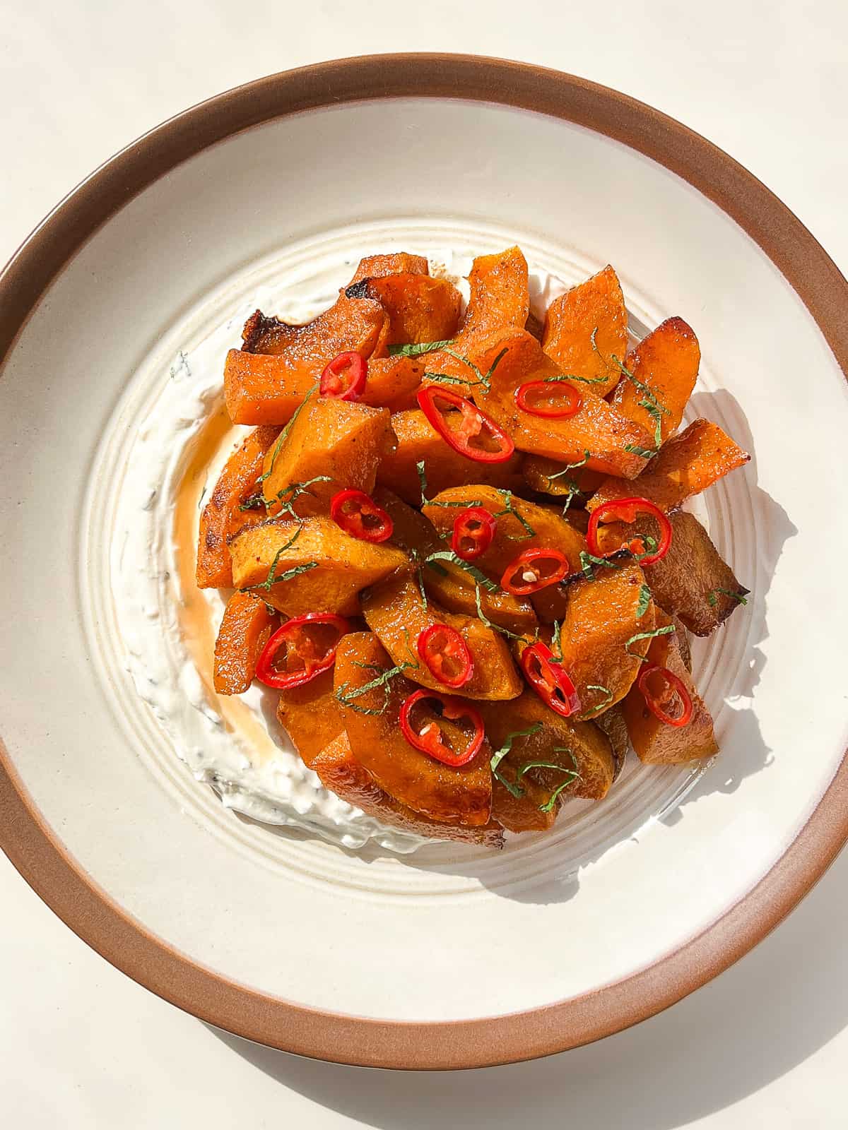 An image of Roasted squash with warm spices, pickled chilies, and lemon mint labneh on a white ceramic plate against a white background.