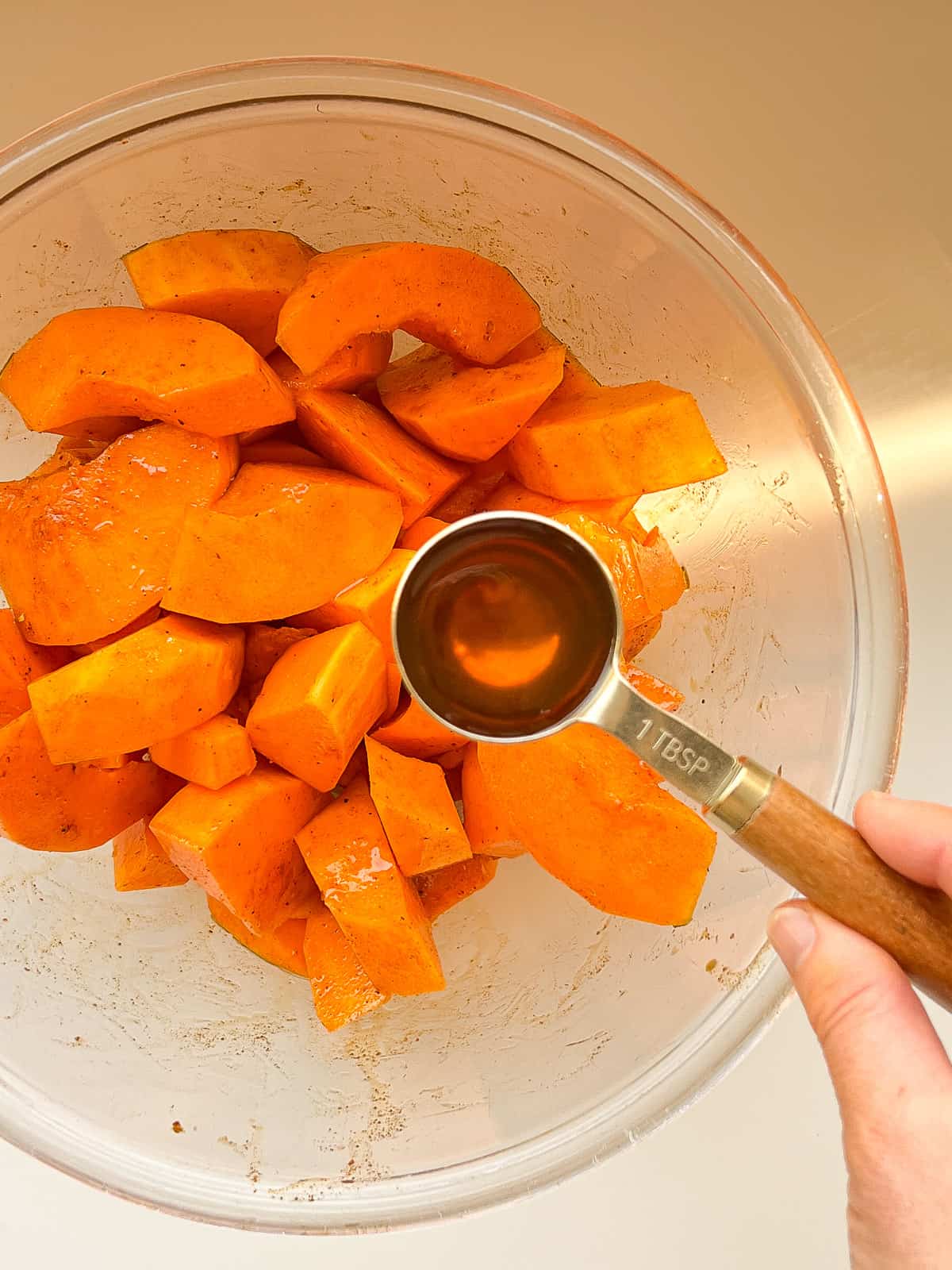 An image of maple syrup being added to a bowl of butternut squash wedges.