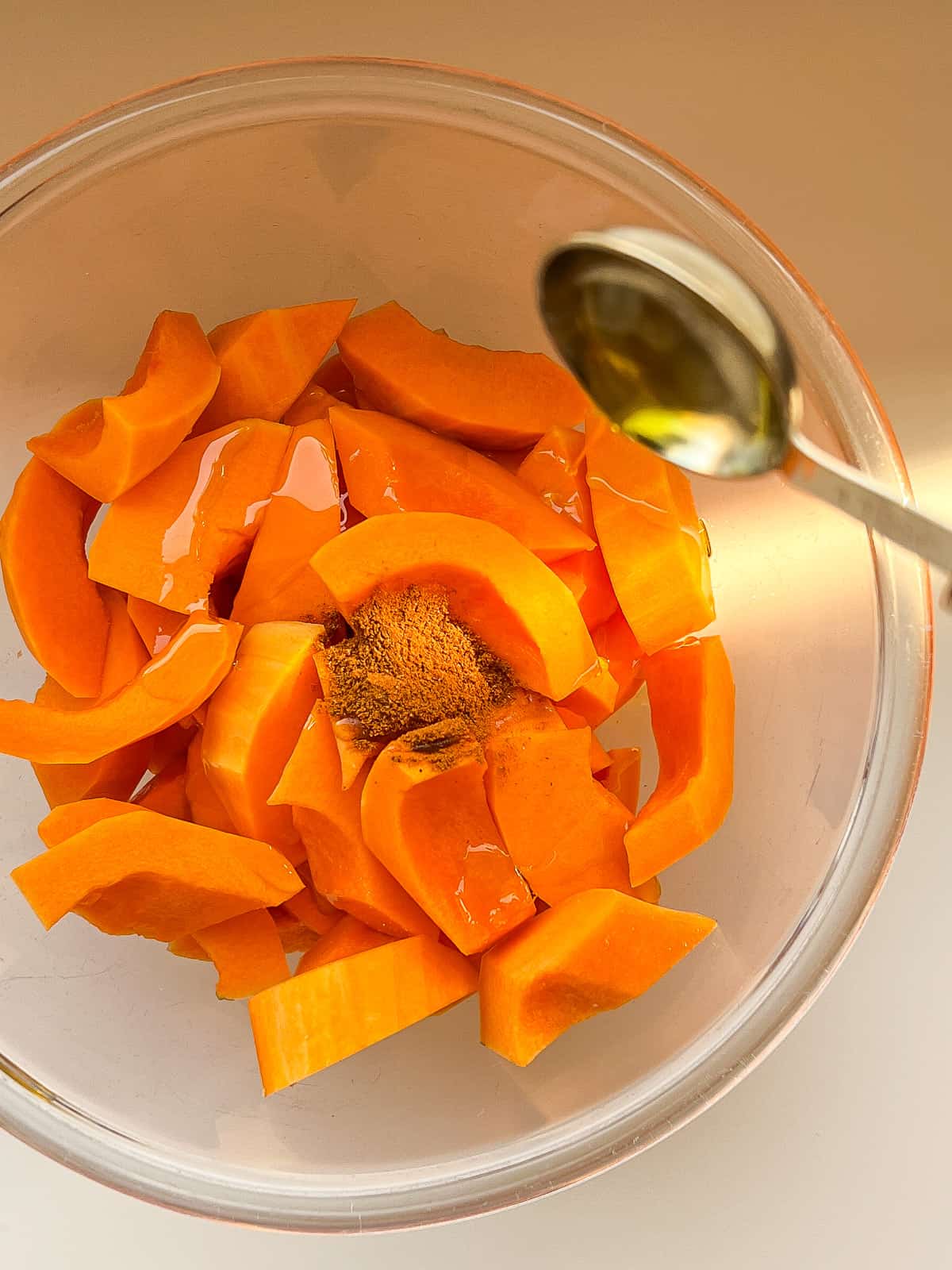 An image of olive oil being added to a bowl of butternut squash wedges.