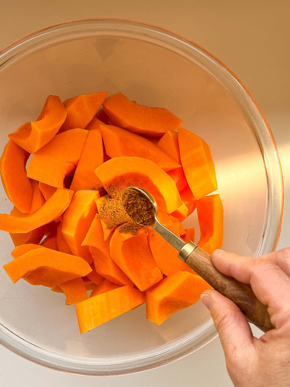 An image of spices being added to a bowl of butternut squash wedges.